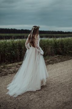 a woman in a white wedding dress walking down a dirt road with her back to the camera