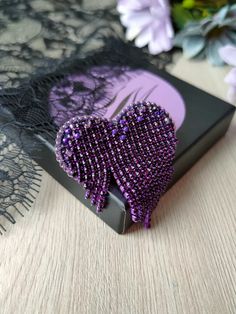 purple beaded heart brooch sitting on top of a black book next to flowers