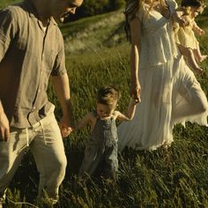 a group of people holding hands and walking through tall grass in an open field,