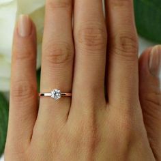 a woman's hand with a diamond ring on top of her finger and white flowers in the background