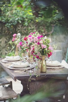 the table is set with pink flowers and gold vases on it's sides