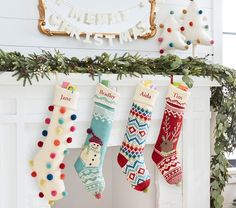 christmas stockings hanging from a mantel decorated with pom - poms and garland