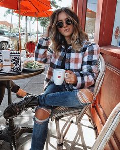 a woman sitting at an outdoor table holding a coffee cup and wearing knee high socks