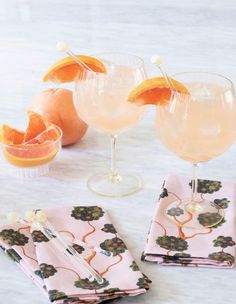 three cocktail glasses with orange slices on the side and napkins next to them sitting on a table