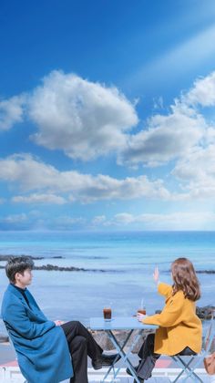 a man and woman sitting at a table with drinks in front of an ocean view