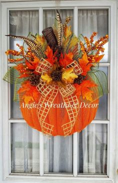 an orange wreath with leaves and flowers on a window sill in front of a white door