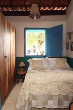 a bed sitting under a window in a bedroom next to a wooden dresser and lamp