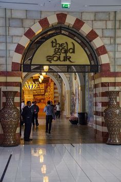 people are walking through an archway in the middle of a shopping mall with large vases on either side