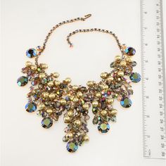 This is part of Chairish’s Costume Jewelry assortment.  Juliana (made by DeLizza & Elster) bib necklace comprised of smoky navette and aurora borealis iridescent rhinestones topped with dangling beads in smoky iridescent and textured gold colors. Setting is gold plated. Unmarked, since only select DeLizza & Elster items were marked with Juliana hang tags. Measures right at 16 inches long; front drop is about 3 inches in the front. Condition is excellent with no missing stones and beautiful gold Elegant Iridescent Necklace For Parties, Iridescent Crystal Necklaces For Party, Elegant Iridescent Crystal Necklaces, Elegant Iridescent Crystal Necklace, Crystal Beaded Necklace With Jewels For Party, Crystal Beaded Necklaces With Jewels For Party, Rhinestone Top, Gold Colors, Bib Necklace