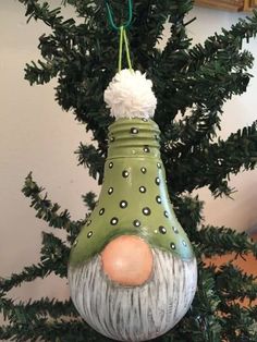 a green ceramic ornament hanging from a tree with pom - poms