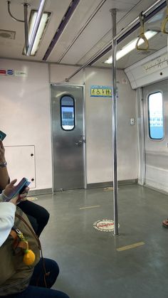 two people sitting on a train looking at their cell phones and reading books in front of them