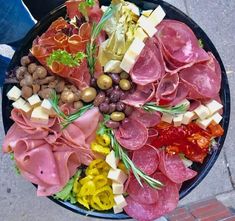 a large platter of meats and cheeses on a black plate next to a person's feet