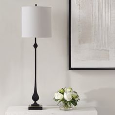 a white vase with flowers on a table next to a black and white lamp in a living room