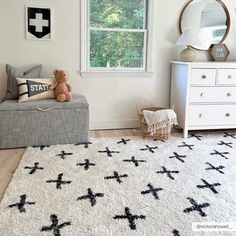 a white and black rug with crosses on it in front of a window next to a dresser