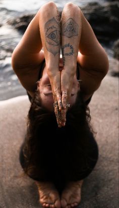 a woman with tattoos on her arms and legs doing a handstand in front of the water