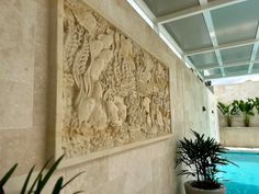 an indoor swimming pool with plants in the foreground and stone carvings on the wall