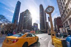 a yellow taxi cab driving down a street next to tall buildings and a clock tower