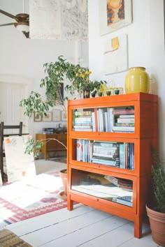 a bookshelf in the corner of a room with potted plants and pictures on the wall