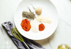 spices and whisks on a white plate next to a glass of wine