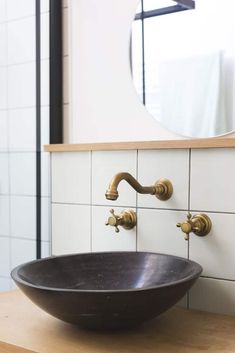 a black bowl sink sitting on top of a wooden counter next to a white tiled wall