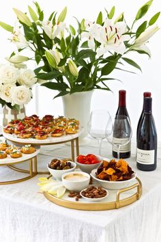 a table topped with plates and bowls filled with food next to bottles of wine on top of a white table cloth