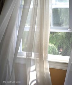 a window with white curtains in front of it and a cat sitting on the window sill