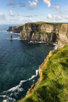 an ocean cliff with green grass on the side and blue water in the foreground