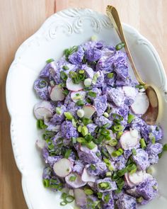 a white bowl filled with purple and green vegetables on top of a wooden table next to a spoon