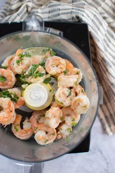 shrimp in a food processor with herbs and lemon wedges on the side for garnish