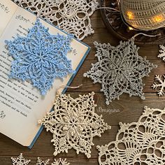 an open book with crocheted snowflakes on it next to a candle