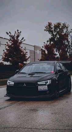 a black car parked on the side of a road in front of some trees and buildings