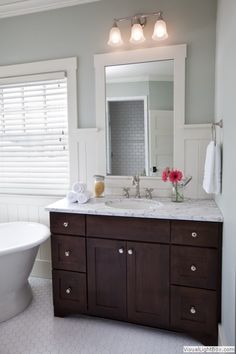 a white bath tub sitting next to a sink under a bathroom mirror with two lights on it