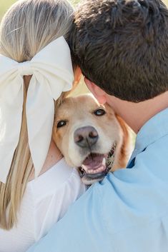 a man and woman hugging their dog with a big white bow on his head in front of them