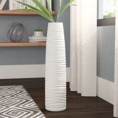 a tall white vase sitting on top of a hard wood floor next to a window