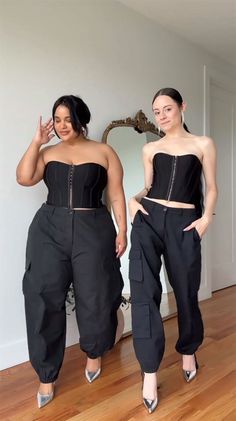 two women standing in front of a mirror wearing black pants with zippers on them