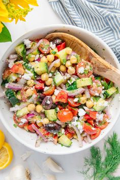 a white bowl filled with chickpeas, cucumbers and onions next to lemons