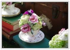 flowers in a teacup on a table with other books and vases behind them