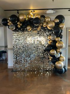 black, gold and silver balloons are hanging from the ceiling in front of a mirror wall