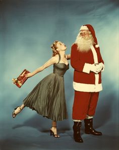 a man dressed as santa claus standing next to a woman in a dress and heels