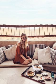 a woman sitting on top of a couch next to a tray with food and drinks