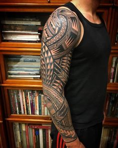 a man's arm with tattoos on it and bookshelves in the background