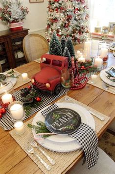 a table set for christmas with plates, candles and decorations on the dining room table