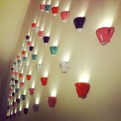 several different colored cups are hanging on the wall next to each other with lights behind them