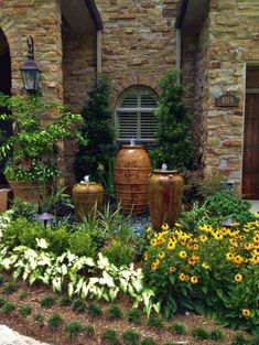 a garden with yellow flowers and large vases in front of a brick building on a sunny day