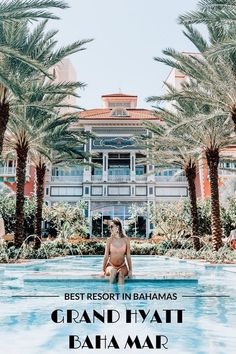 a woman sitting on the edge of a swimming pool in front of a hotel with palm trees