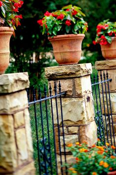 three flower pots on top of stone pillars in front of a fence with flowers growing out of them