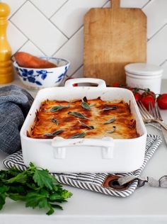 a casserole dish on a kitchen counter with tomatoes, carrots and parsley