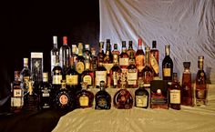 there are many different types of liquor on the table and behind them is a white sheet