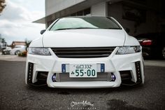 the front end of a white car parked in a parking lot next to a building