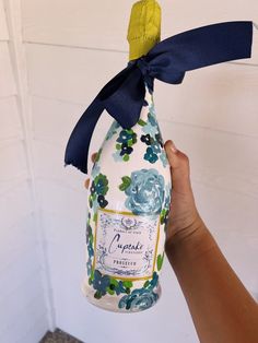 a hand holding up a bottle that is decorated with flowers and blue ribbon on it